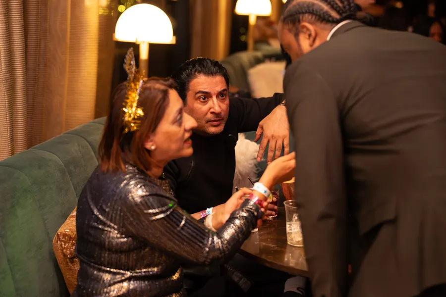 Guests at a New Year's Eve lounge party, one in a metallic sequin top and gold tiara, another in a dark suit jacket