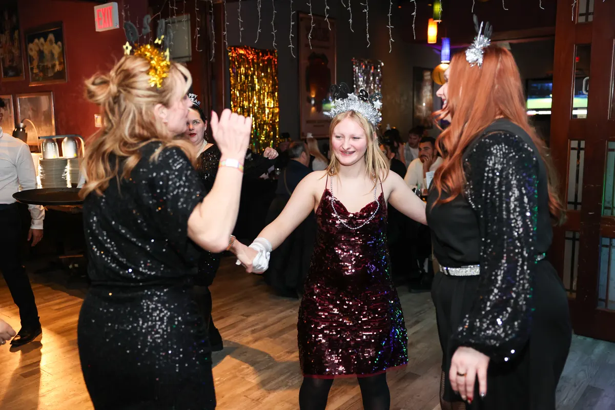 Guests in black and burgundy sequin dresses and sparkly tiaras dancing at a New Year's Eve party
